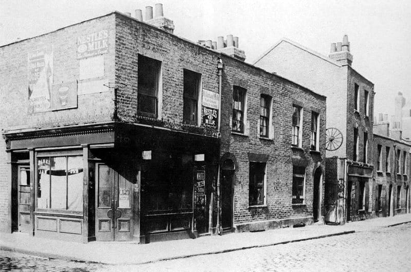 Berner Street in 1909, a row of brick houses with a cartwheel sign hanging over the entrance to Dutfield's Yard