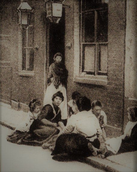 Women and children sitting on a doorstep in an East End street around 1890